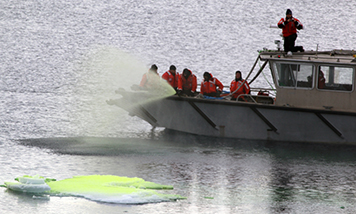 People spray green dye from a boat onto water and ice.